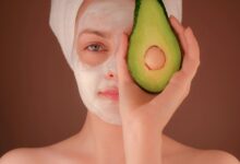 woman with white face mask holding green fruit